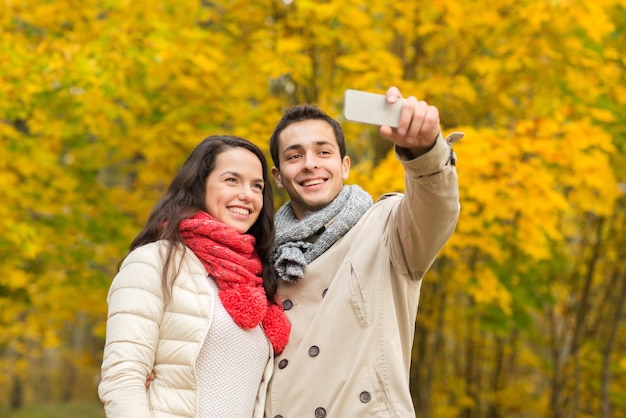 conceito de amor, relacionamento, família e pessoas - casal sorridente abraçando e tirando selfie no parque outono