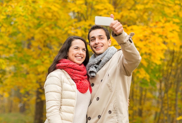 conceito de amor, relacionamento, família e pessoas - casal sorridente abraçando e tirando selfie no parque outono