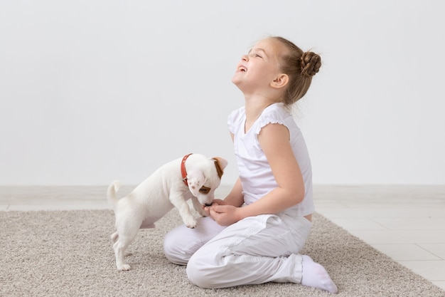 Conceito de animais, crianças e animais de estimação - menina criança sentada no chão com o cachorrinho fofo e brincando.