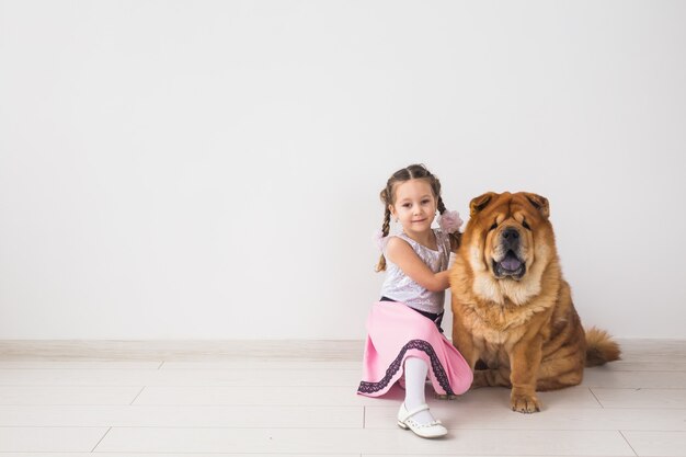 Conceito de animais de estimação, crianças e amizade - menina abraçando seu cachorro chow-chow sobre uma parede branca