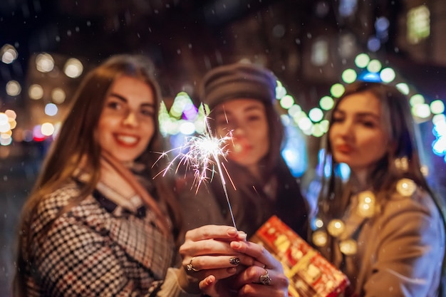 Conceito de ano novo. mulheres amigas queimando fogos de artifício em lviv, na feira de rua, se divertindo com presentes. meninas comemorando feriados sob a neve