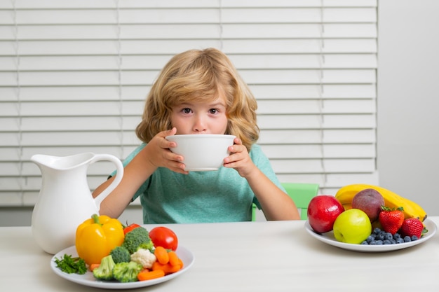 Conceito de apetite de fome garoto comendo alimentos saudáveis vegetais café da manhã com frutas de leite e vegetais