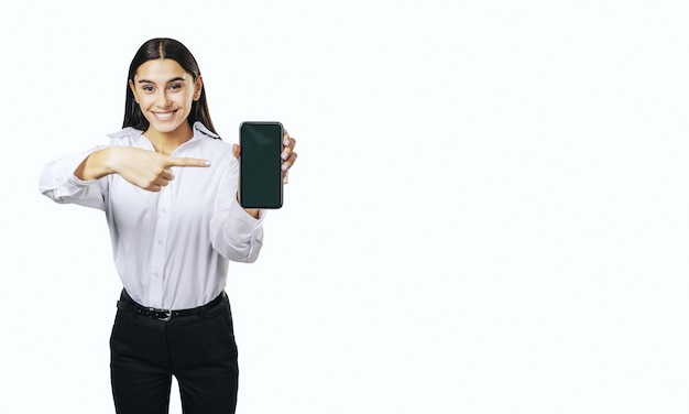 Conceito de aplicativo móvel com garota feliz na camisa branca mostrando smartphone moderno com tela em branco isolada no fundo branco com lugar para o seu logotipo ou maquete de texto