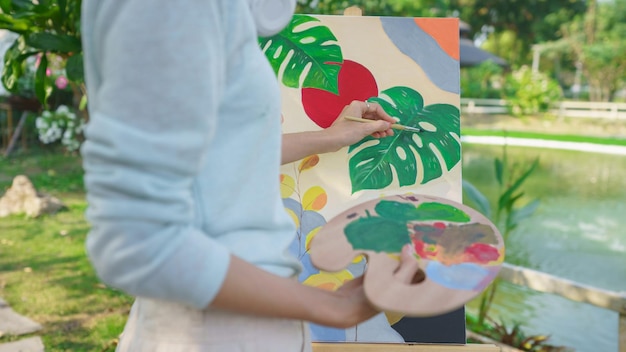 Conceito de artista artista feminina segurando paleta de cores e pintando imagens em tela no jardim