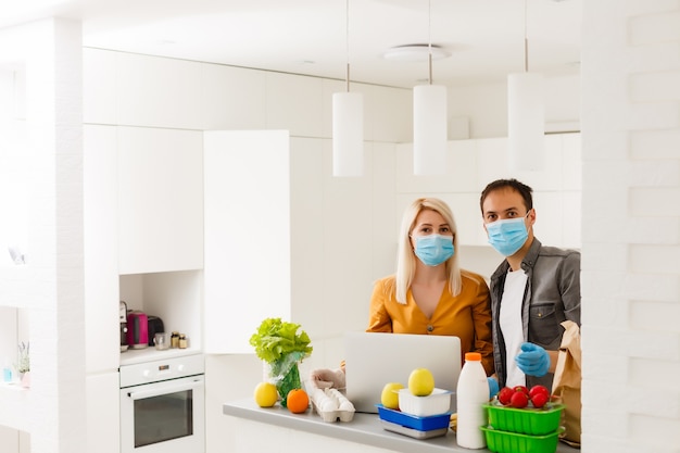 Conceito de auto-isolamento. casal desempacotando saco de papel com comida na cozinha, pronto para quarentena durante o surto epidêmico