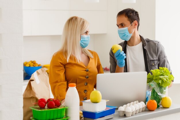 Conceito de auto-isolamento. casal desempacotando saco de papel com comida na cozinha, pronto para quarentena durante o surto epidêmico