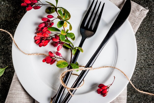 Conceito de backgorund de comida de outono Jantar de ação de graças Mesa de pedra escura com conjunto de garfo de faca talheres com bagas de outono como decoração Fundo preto