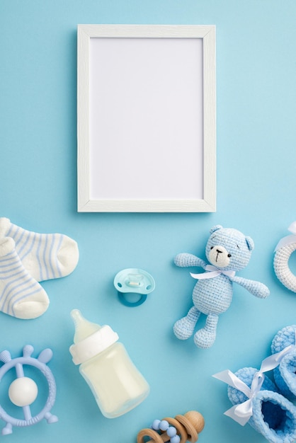 Conceito de bebê menino Vista superior foto vertical de meias de garrafa de moldura de foto ursinho de malha botas de brinquedo mordedor chocalho de madeira e chupeta em fundo azul pastel isolado com espaço vazio