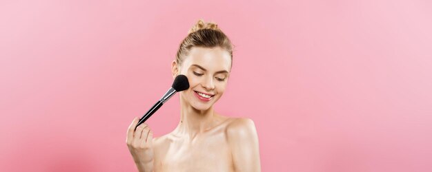 Conceito de beleza Closeup Linda mulher caucasiana aplicando maquiagem com pincel de pó cosmético Pele perfeita isolada em fundo rosa e espaço de cópia