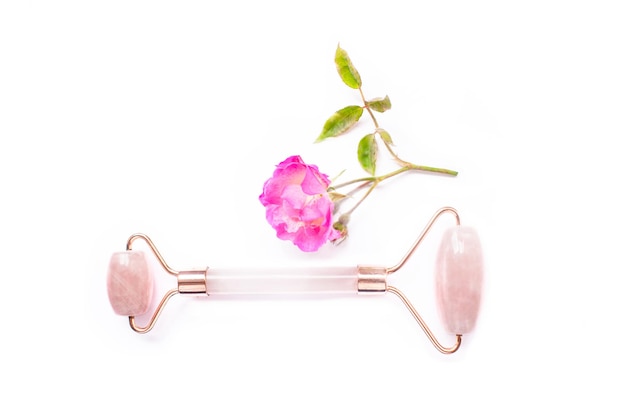 Conceito de beleza e cuidados com a pele com um massageador facial de quartzo rosa acompanhado por uma flor rosa