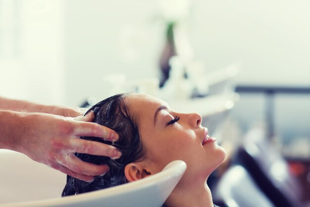 conceito de beleza e pessoas - jovem feliz com cabeleireiro lavando a cabeça no salão de cabeleireiros