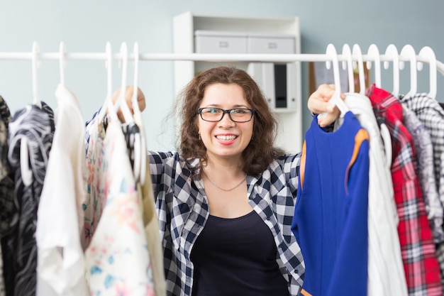 Conceito de beleza, moda e pessoas - linda mulher sorridente em óculos escuros escolhe vestidos