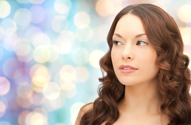 Conceito de beleza, pessoas e saúde - rosto de mulher jovem e bonita sobre fundo azul de luzes de feriados