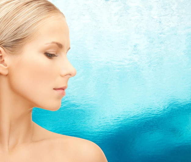 Foto conceito de beleza, pessoas e saúde - rosto de mulher jovem e bonita sobre fundo de água azul ondulada