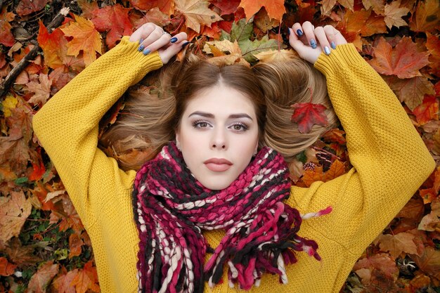 Conceito de beleza, pessoas, estação e saúde - menina bonita deitada em folhas de outono vermelhas e amarelas