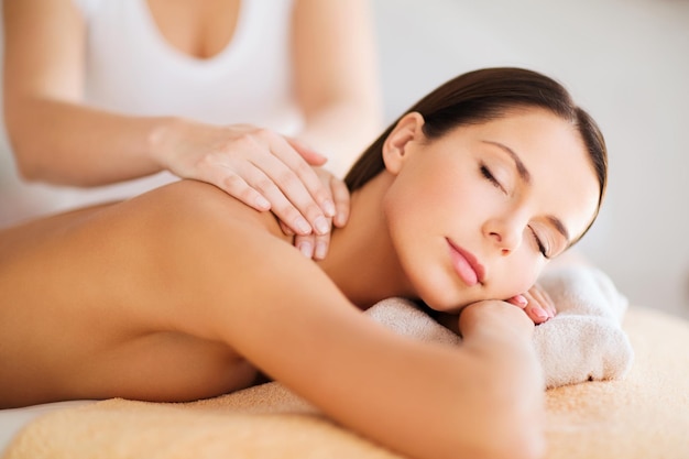 conceito de beleza, spa, resort e relaxamento - mulher bonita em salão de spa recebendo massagem