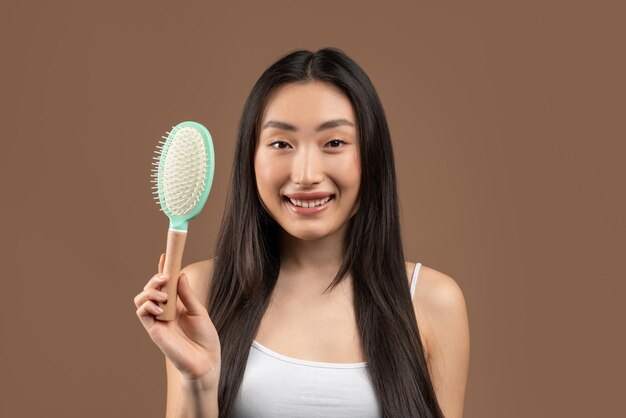 Conceito de cabelo saudável e bonito mulher coreana feliz com cabelos longos e sedosos segurando escova e sorrindo