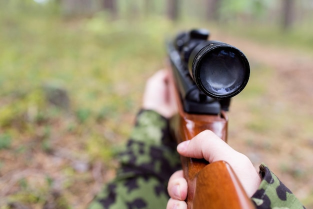 conceito de caça, guerra, exército e pessoas - close-up de jovem soldado, ranger ou caçador com arma na floresta