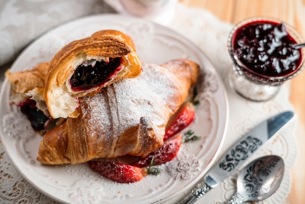 Conceito de café da manhã com uma xícara de café, croissants, creme e frutas frescas.