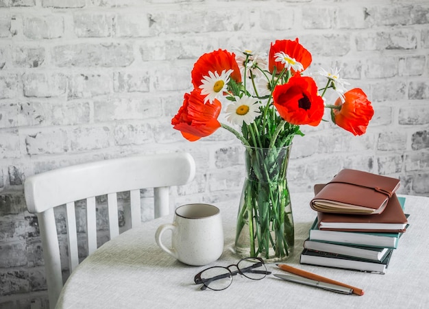 Conceito de casa interior acolhedor Bouquet de margaridas de papoilas pilha de livros xícara de chá em uma mesa