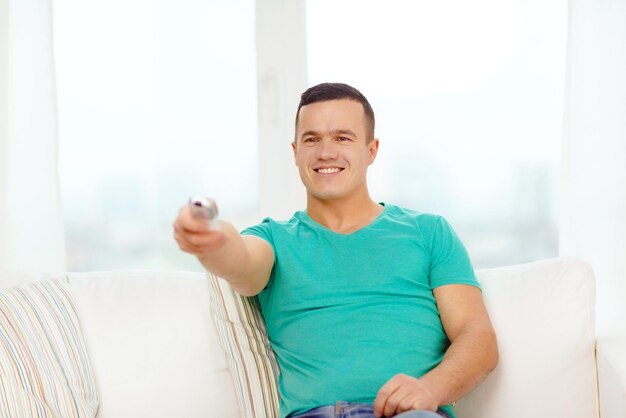 conceito de casa, tecnologia e entretenimento - homem sorridente com controle remoto de tv em casa