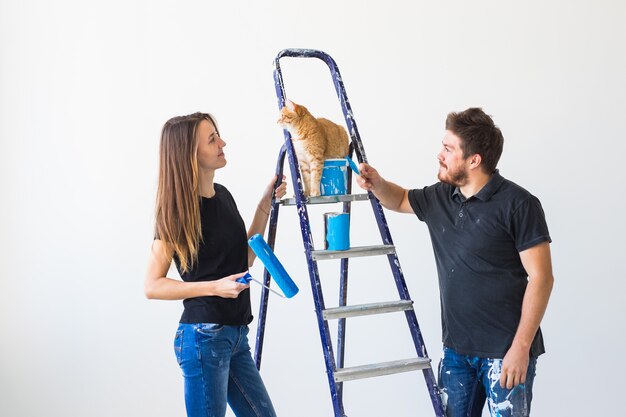 Conceito de casal de reparação, renovação, animal de estimação e amor - família jovem com gato fazendo reparos e pintando paredes juntos e rindo.