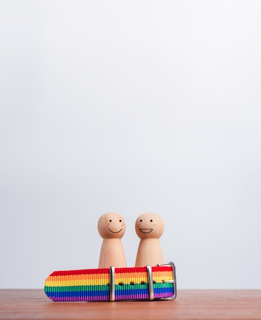 Conceito de casal lgbt. duas figuras de madeira com sorrisos felizes juntos na bandeira do arco-íris, pulseira na mesa de madeira e fundo com espaço de cópia, estilo vertical. símbolo do orgulho lgbt.