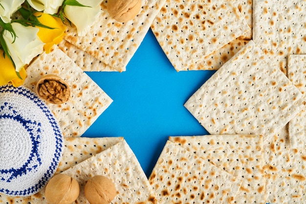 Conceito de celebração da Páscoa Azul Estrela de Davi feita de matzah rosas brancas e amarelas kipá e noz em fundo azul Ritual tradicional Comida judaica da Páscoa Pessach Feriado judaico Mock up