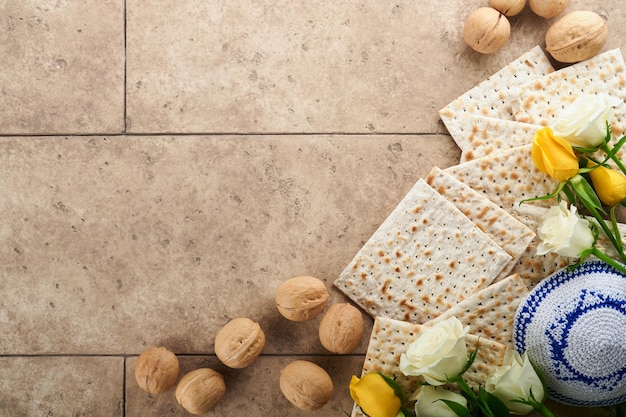 Conceito de celebração da Páscoa Matzah kosher vinho tinto noz e rosas brancas e amarelas Ritual tradicional Pão judaico em fundo de parede de azulejo antigo de cor de areia Comida de Páscoa Feriado judaico de Pessach