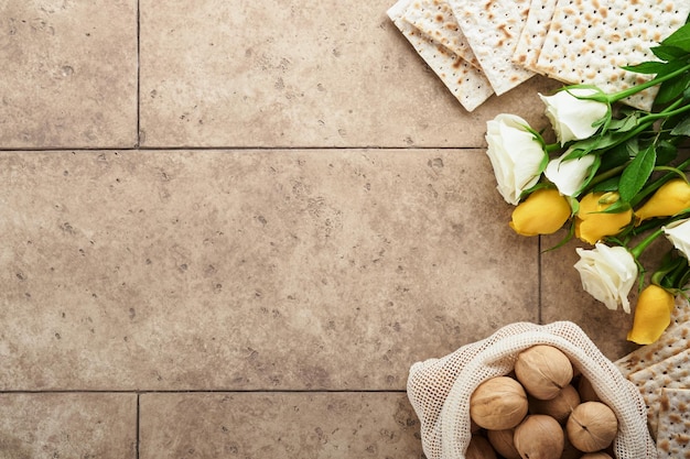 Conceito de celebração da Páscoa Matzah kosher vinho tinto noz e rosas brancas e amarelas Ritual tradicional Pão judaico em fundo de parede de azulejo antigo de cor de areia Comida de Páscoa Feriado judaico de Pessach