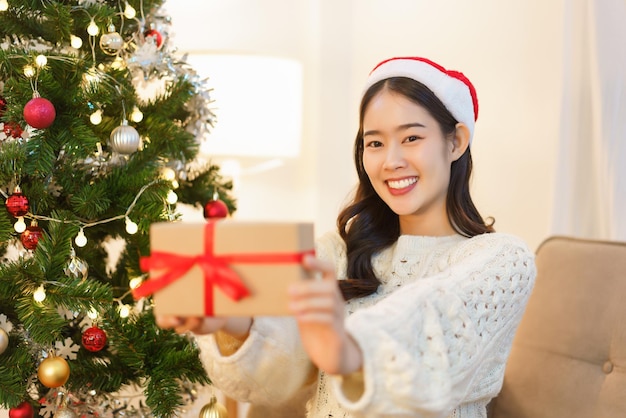 Conceito de celebração de natal jovem asiática com chapéu de papai noel sorrindo e segurando presente de natal