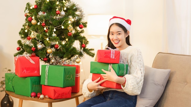 Conceito de celebração de natal Jovem mulher asiática sentada no sofá e segurando presentes de natal