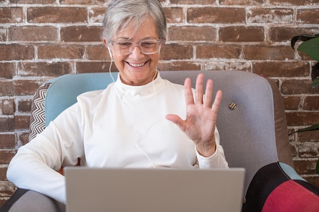 Conceito de chamada de vídeo Mulher aposentada feliz acenando com as mãos Chamadas de vídeo por laptop