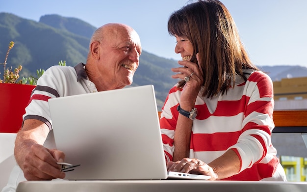 Conceito de chamada de vídeo sorrindo adorável casal sênior sentado ao ar livre usando computador laptop juntos