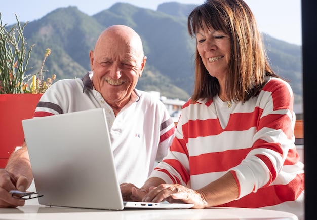 Foto conceito de chamada de vídeo sorrindo adorável casal sênior sentado ao ar livre usando computador laptop juntos