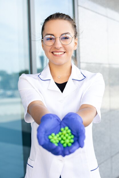 Conceito de ciência, química, biologia e medicina - Cientista oriental sorridente com um jaleco branco, óculos e luvas de borracha, mostrando moléculas verdes nas mãos e olhando para longe em uma área externa