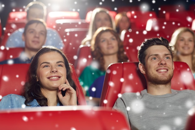 Foto conceito de cinema, entretenimento e pessoas - amigos felizes assistindo filme no teatro com flocos de neve