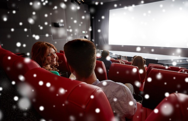 Foto conceito de cinema, entretenimento e pessoas - amigos felizes ou casal assistindo filme no teatro na última fila e falando de volta sobre flocos de neve