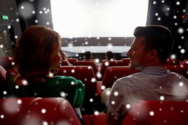 Foto conceito de cinema, entretenimento e pessoas - amigos felizes ou casal assistindo filme no teatro na última fila e falando de volta sobre flocos de neve