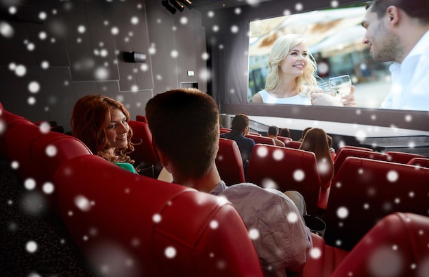 Foto conceito de cinema, entretenimento e pessoas - amigos felizes ou casal assistindo filme no teatro na última fila e falando de volta sobre flocos de neve