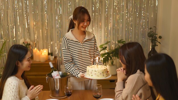 Foto conceito de comemoração de aniversário meninas asiáticas fazem um desejo enquanto recebem bolo de aniversário de amigos