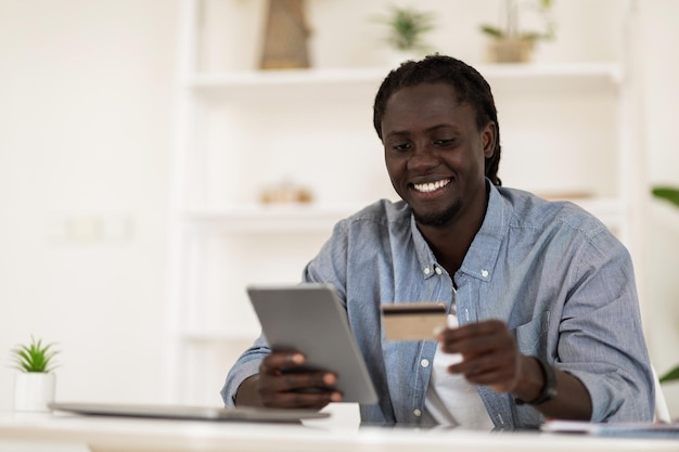 Conceito de comércio eletrônico sorrindo homem negro usando tablet digital e cartão de crédito