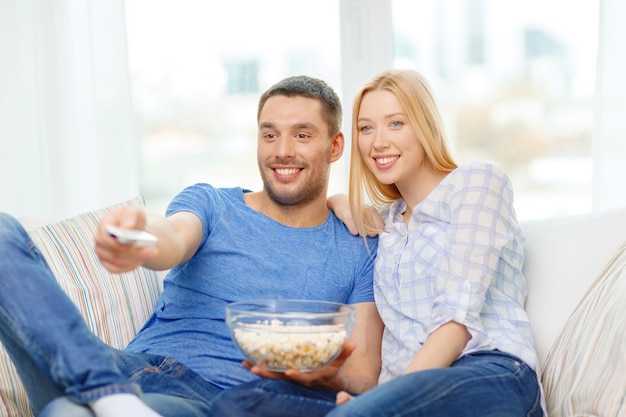 conceito de comida, amor, família e felicidade - casal sorridente com pipoca assistindo filme em casa