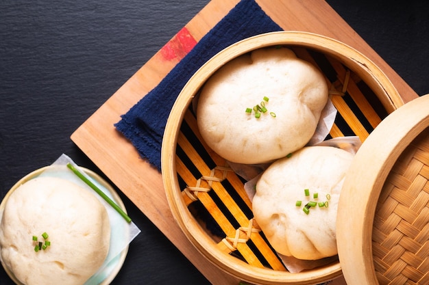 Conceito de comida asiática bolinho de carne chinês baozi em vapor de bambu dim sum na placa de madeira no fundo de pedra ardósia preta com espaço de cópia