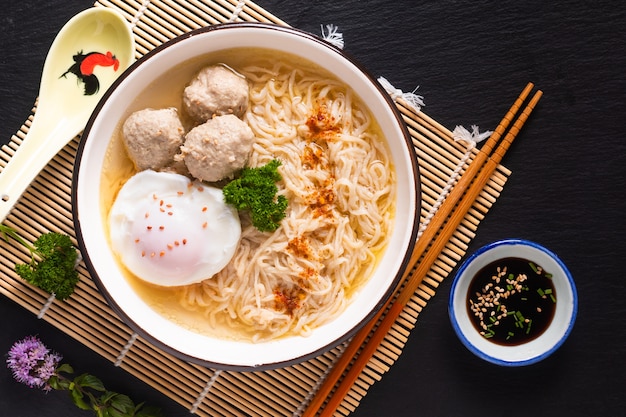 Conceito de comida asiática Macarrão de ovo Ramen Estilo asiático com almôndega no fundo preto fosco de bambu com espaço de cópia