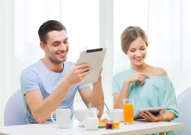 conceito de comida, casa, casal e tecnologia - casal sorridente com tablet pc lendo notícias e tomando café da manhã em casa