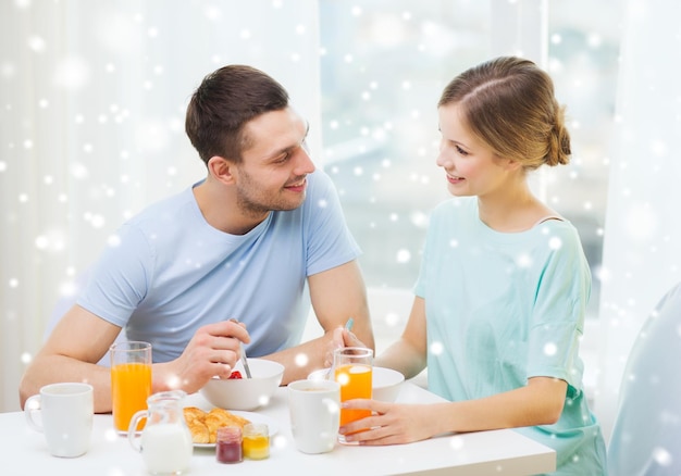 conceito de comida, casa, pessoas e felicidade - casal sorridente tomando café da manhã em casa