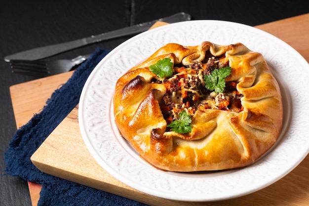 Conceito de comida caseira rústica torta de carne moída Galette em chapa branca na placa de madeira com espaço de cópia