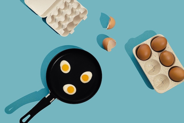 Conceito de comida criativa com ovo frito gomoso em forma de casca de ovo em uma frigideira preta sobre fundo azul Vista superior do café da manhã da manhã Estilo mínimo padrão sem costura Postura plana