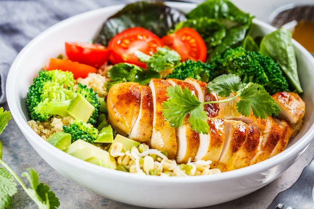 Conceito de comida equilibrada. Salada de frango, brócolis e quinoa em tigela branca, fundo cinza.